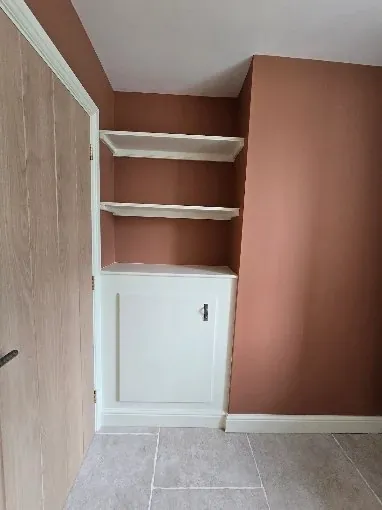 Alcove shelving and cupboard painted white against a terracotta wall